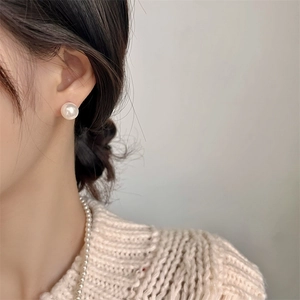 Close-up of elegant 8-10mm white pearl stud earring worn with a knitted sweater