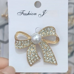 Détail d'une broche nœud dorée ornée de strass brillants et d'un insert central en perle