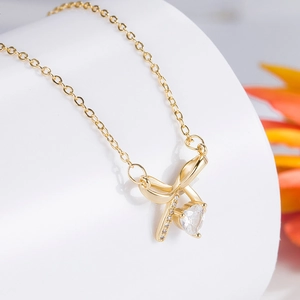 Elegant gold bow necklace with heart-shaped crystal pendant on white display stand