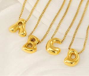 Detailed view of four golden bubble letter necklaces A B C D on a white background