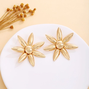 Detailed close-up of large golden floral earrings with 3D petals on a white tray