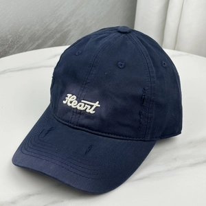 Macro detail of white 'Heart' embroidery and distressed ripped brim on navy baseball cap