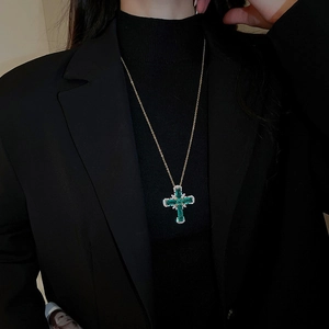 Gros plan d'un collier croix doré avec pierre vert émeraude sur un mannequin en costume
