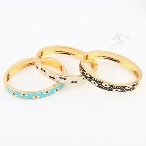 Detailed view of three gold-plated enamel Evil Eye bangles in blue, white, and black