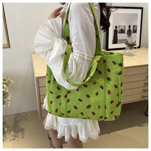 Detailed texture of green corduroy tote bag with strawberry print and wide strap