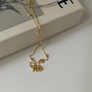 Minimalist gold beaded cross chain necklace in 925 sterling silver on a grey book background