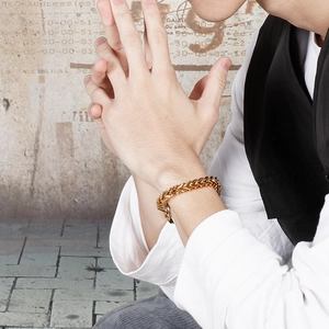 Close-up of a gold-toned men's braided keel chain bracelet on a wrist with textured background