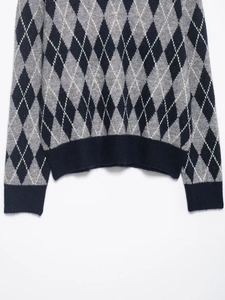 Detail of argyle knit sweater showing ribbed cuffs and hem in navy and grey texture