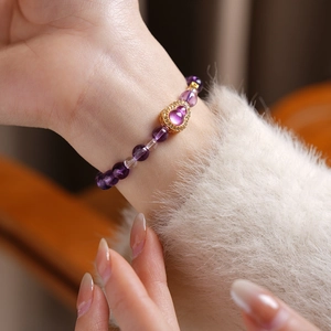 Close-up of purple crystal bead bracelet with a gold heart pendant and gemstone on a wrist
