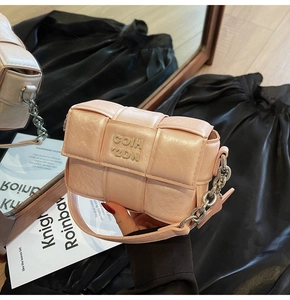 Détail du sac bandoulière tressé rose avec chaîne métallique et logo décoratif
