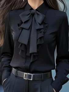Detail of black satin shirt featuring ruffle collar and a large elegant bow tie accent