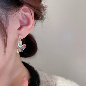 Close-up of gold-plated heart earrings with red and iridescent crystals on a model