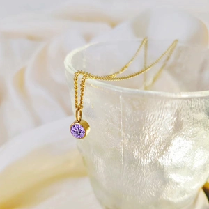Detailweergave van een gouden ketting met ronde paarse geboortesteen hanger op een glas