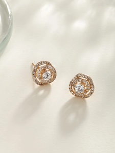 Macro dettaglio di orecchini a spirale in oro rosa con pavé di zirconi e cristallo centrale
