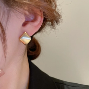 Détail d'une boucle d'oreille carrée en or brossé portée par un mannequin, effet mat