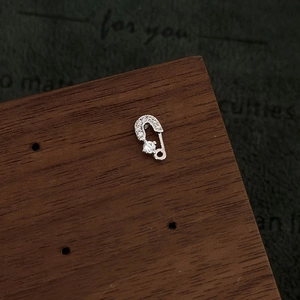 Close-up of a silver safety pin earring with micro-set zircons on dark background