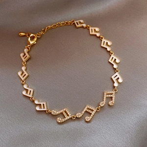 Macro view of gold music note bracelet with zircons and enamel on grey silk fabric