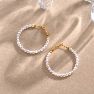 Macro shot of gold C-shaped hoop earrings with white pearls on a sandy background
