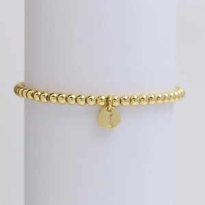 Detailed macro view of golden beaded bracelet with a polished initial letter I pendant