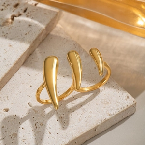 Bague griffe en métal liquide doré en acier inoxydable sur une pierre texturée beige