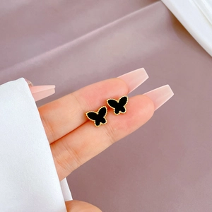 Macro shot of butterfly stud earrings with golden edges and black inlay held by hand