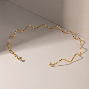 Nahaufnahme des goldenen, wellenförmigen Edelstahl-Halsreifs auf weißem Grund
