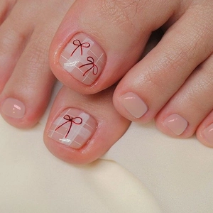 Macro detail of nude plaid toe nail patches with cute red bow designs for women