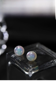 Macro view of round iridescent pearl stud earrings with dreamlike rainbow shimmer