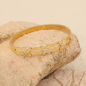 Dettaglio del bracciale dorato con maglie a X e cristalli pavé su una pietra decorativa
