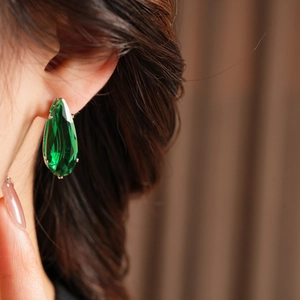 Close-up of deep green teardrop zircon earrings with silver claws on model's ear
