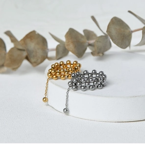 Close-up of gold and silver beaded rings with dangling chain charms on a white stand