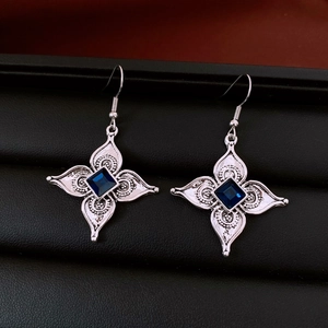 Détail des boucles d'oreilles fleur argentée avec pierre bleue sur support en cuir noir
