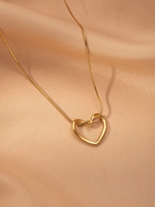 Detail of a golden heart pendant on a stylish snake chain over champagne silk fabric