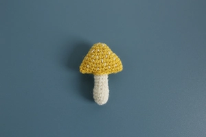 Detail of handmade crochet mushroom brooch with white spots on yellow cap