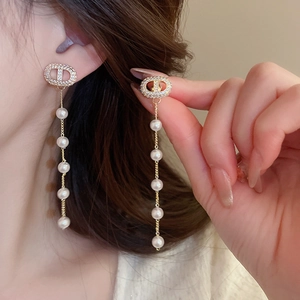 Detailed close-up of gold tassel earrings with pearls and pavé stones on a model