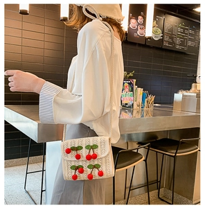 Detailed view of handmade straw woven crossbody bag with cute 3D cherry decor