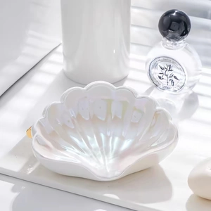 Dettaglio del portasapone in ceramica a forma di conchiglia con finitura perlata e bordo oro