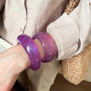 Detail of purple resin bangles with glitter insets worn in an aesthetic lifestyle setting