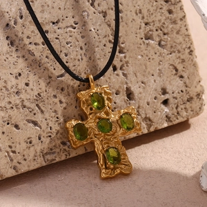 Close-up of a 18K gold-plated cross pendant with green emerald stones on a stone surface