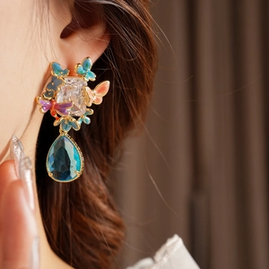 Close-up of vintage earrings featuring colorful enamel butterflies and a blue teardrop stone