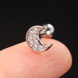 Macro shot of a tiny zircon-inlaid moon cartilage stud held on a fingertip for size