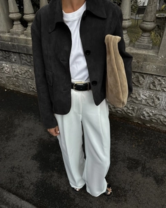 Street style view of a black suede jacket paired with white wide-leg trousers and a clutch
