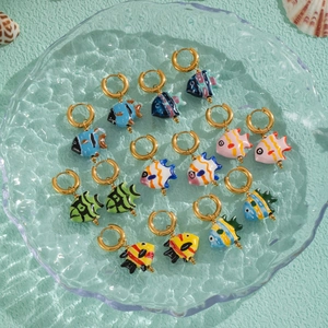 Colorful ceramic koi fish earrings with gold hoops on a green textured surface