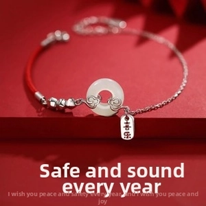 Macro shot of silver bracelet with white jade pendant and engraved tag on red background