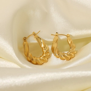 Macro detail of gold-plated twisted hoop earrings on soft yellow satin fabric
