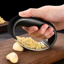 Close-up of a stainless steel garlic press mincing cloves on a wooden cutting board