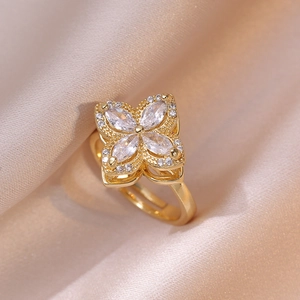 Golden rotating four-leaf clover ring with zircon stones on pink satin backdrop
