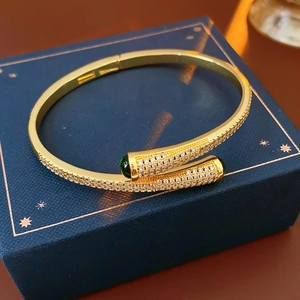 Close-up of gold-plated bangle with pavé zircons and green gemstone ends on jewelry box