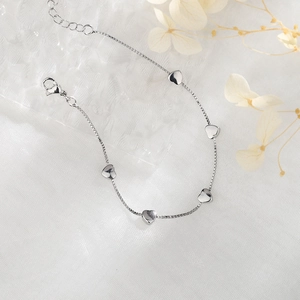 Detailed view of silver heart charms on a box chain bracelet with lobster clasp closure