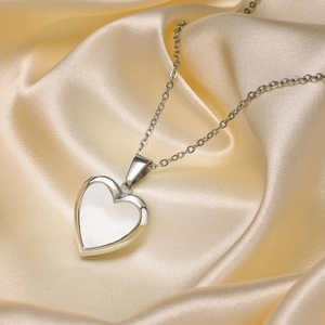 Detailed view of silver heart locket necklace with white shell inlay on champagne satin